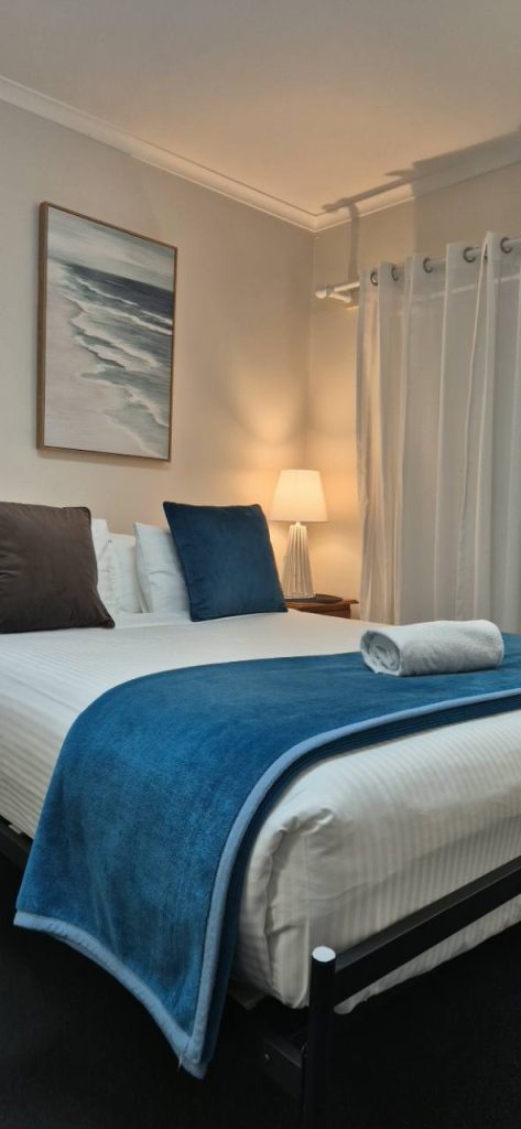 Freshly prepared bed with blue runner and bedside lamp at City Heart Motel Warrnambool